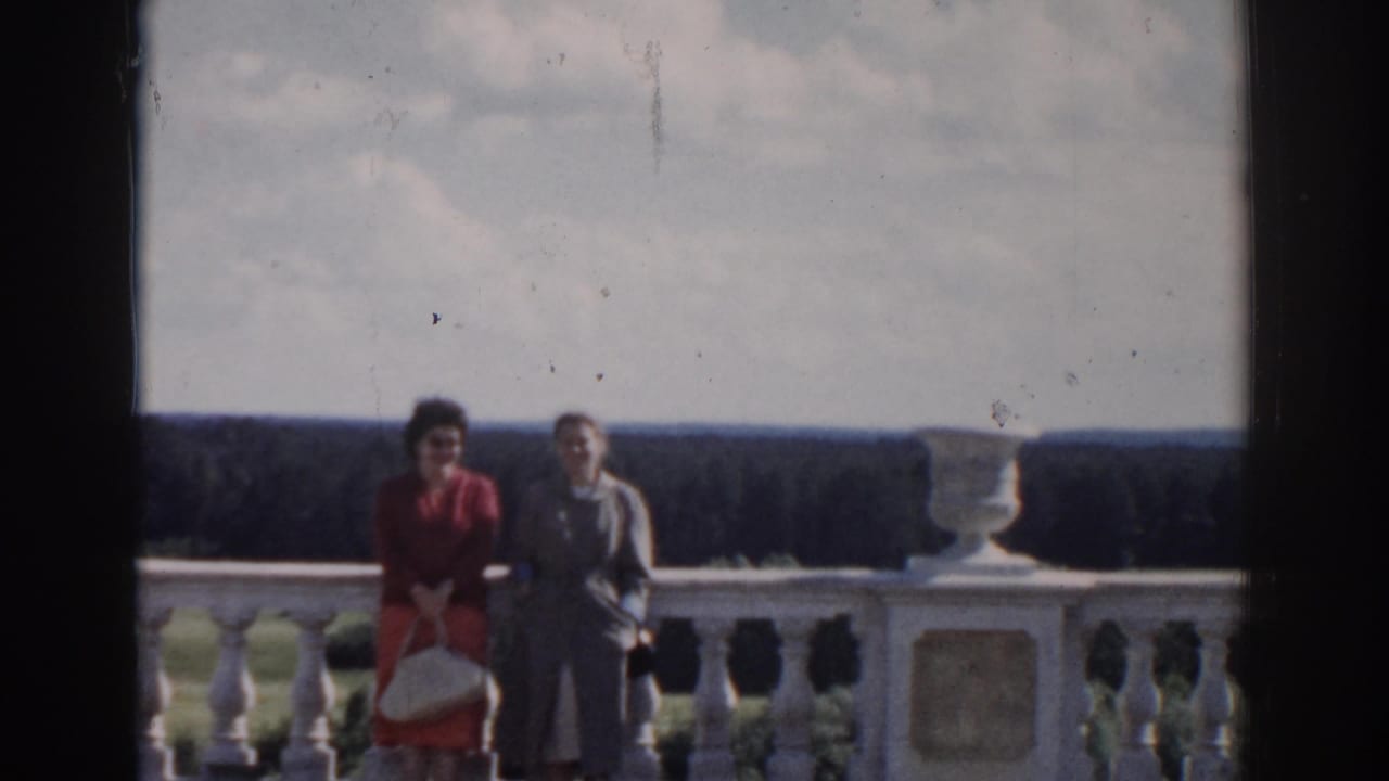 Two women in 1968 Moscow footage pose beside a pale stone balustrade overlooking a broad forested landscape.