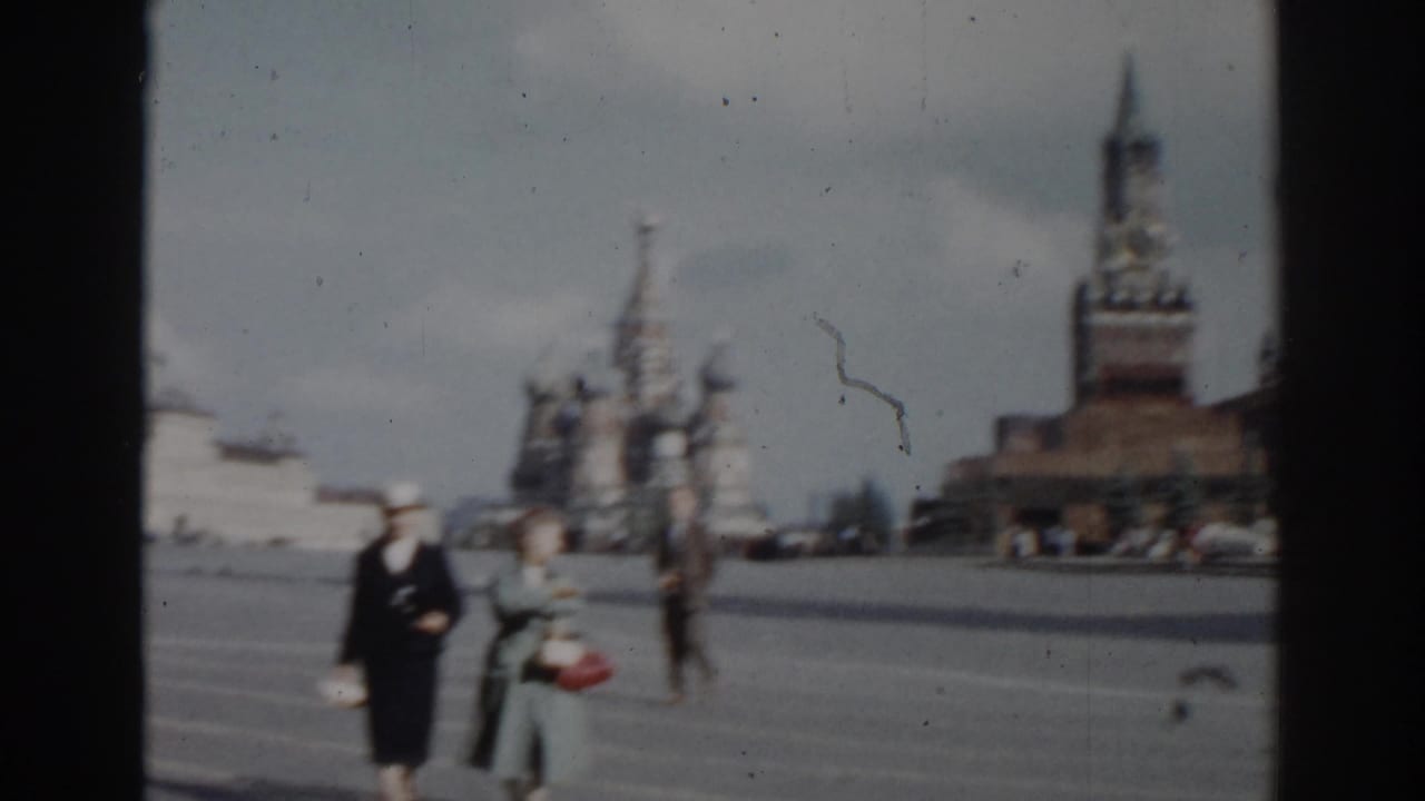 Two women walking across Red Square with cathedral domes and a tower in the background.