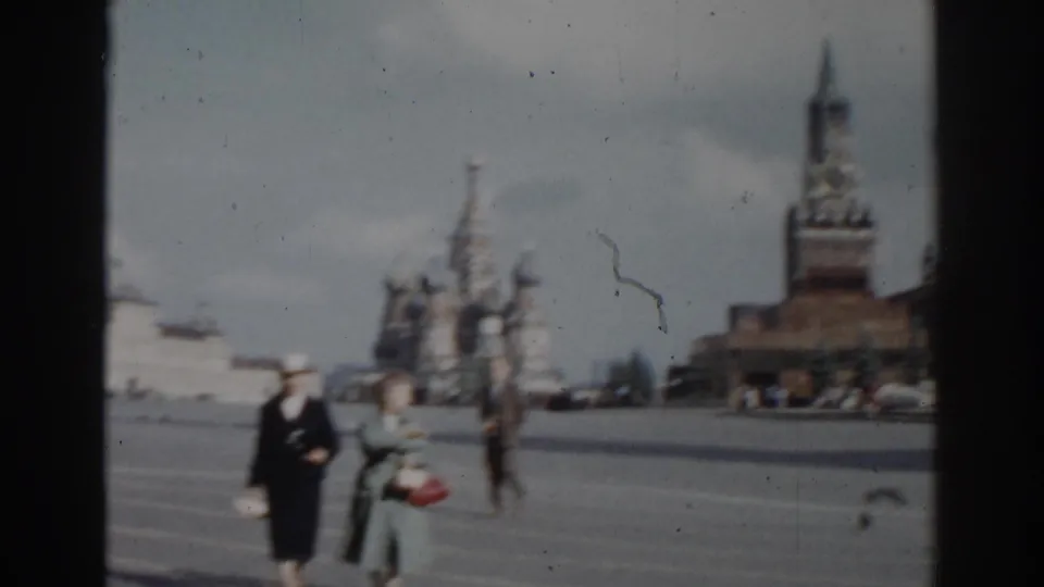 Two women in period coats walk across Red Square in Moscow, with St. Basil's Cathedral and a Kremlin-area tower behind them.