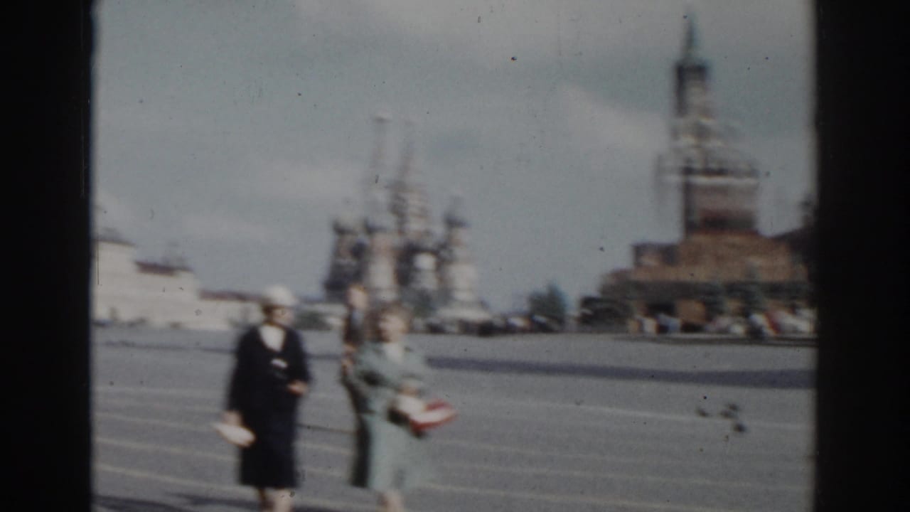 Two women continue walking in the square, with St. Basil's Cathedral behind them.