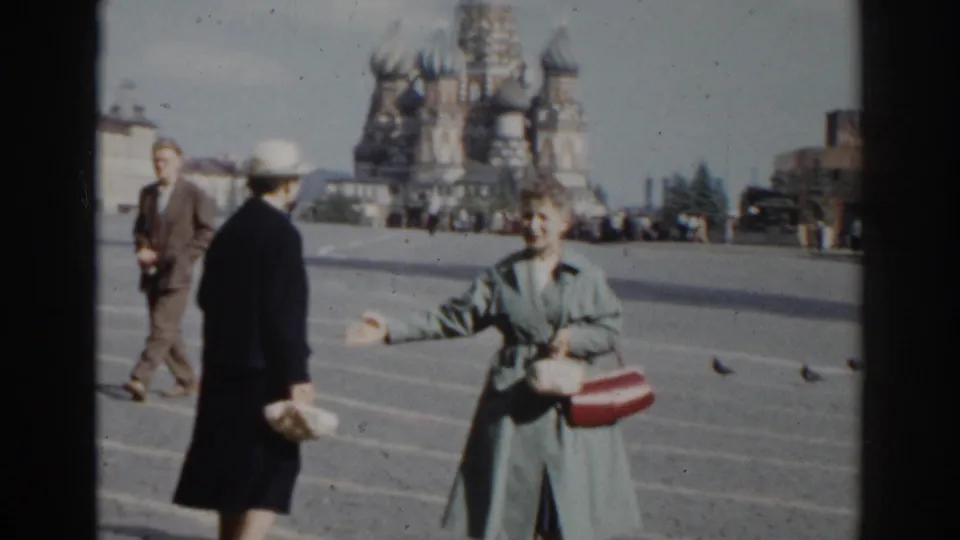 A woman in a blue-gray coat gestures across Red Square while another woman in a dark coat faces her near St. Basil's Cathedral.