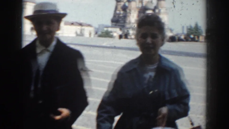 In 1968 Moscow home-movie footage, a suited man in a light hat and a woman with a bag appear close to camera near a public square.