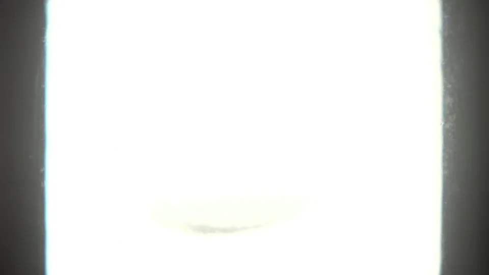A mostly overexposed 8mm frame appears nearly white, bordered by dark film edges and faint trace marks.