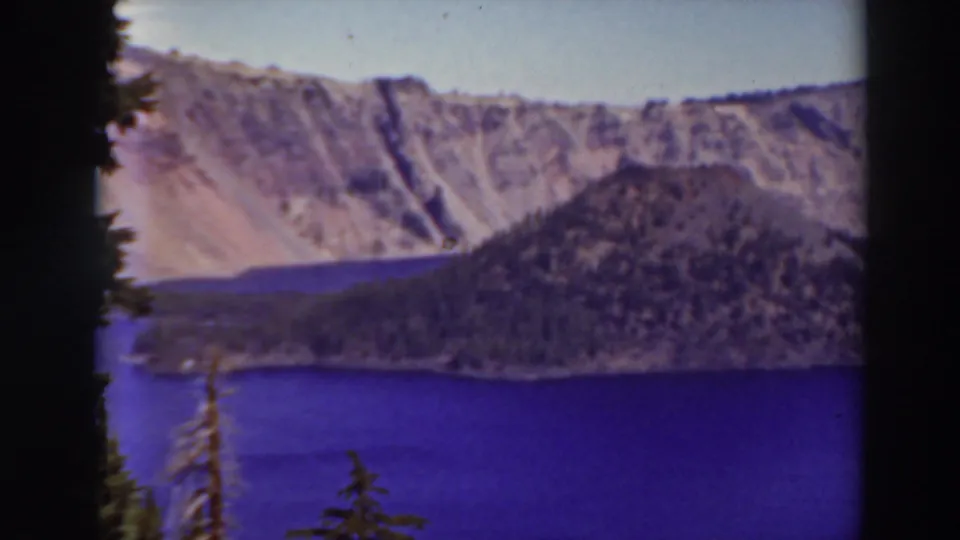 Final 1937 Crater Lake frame holding on blue water, forested shoreline or island slope, pale caldera cliffs, and visible 8mm gate edges.