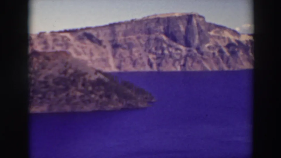 1937 aerial home-movie frame of Crater Lake with the caldera wall across the horizon and blue water below.