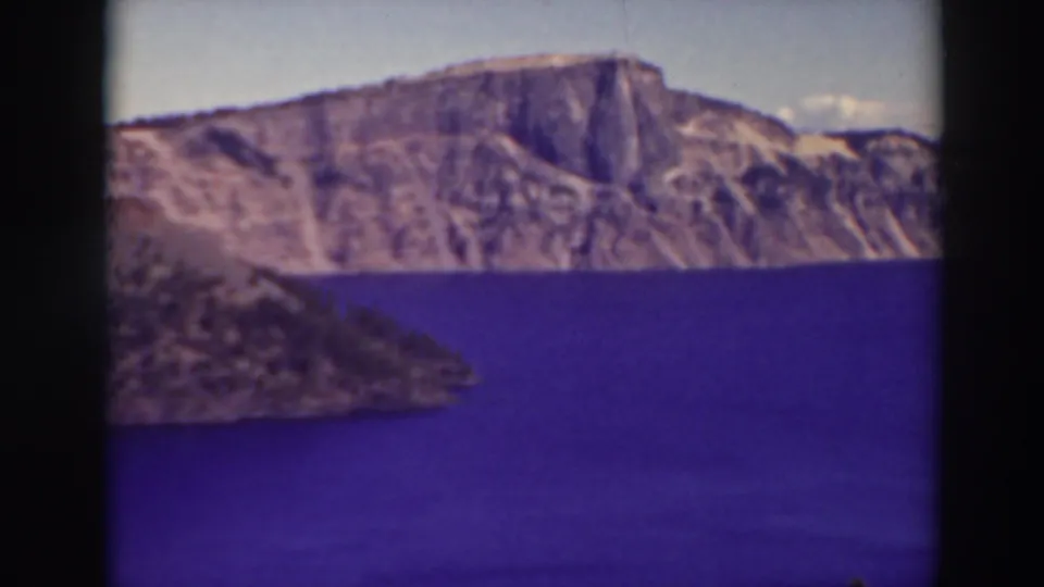 Soft 8mm aerial view of Crater Lake, Oregon, with blue water, rocky island edge, and rugged caldera wall.