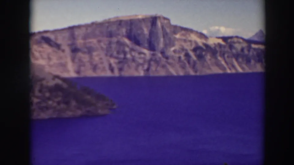 1937 8mm view of Crater Lake, Oregon, showing deep blue water, caldera cliffs, and a dark foreground slope.