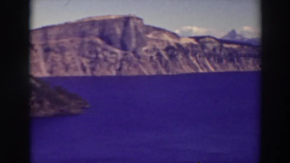Crater Lake, Oregon, appears in a soft 1937 8mm frame with blue water, pale rim cliffs, and distant peaks.