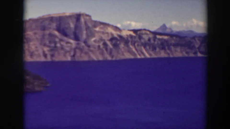 Metadata-supported 1937 Crater Lake view with soft-focus volcanic cliffs, blue water, and a small dark slope at lower left.