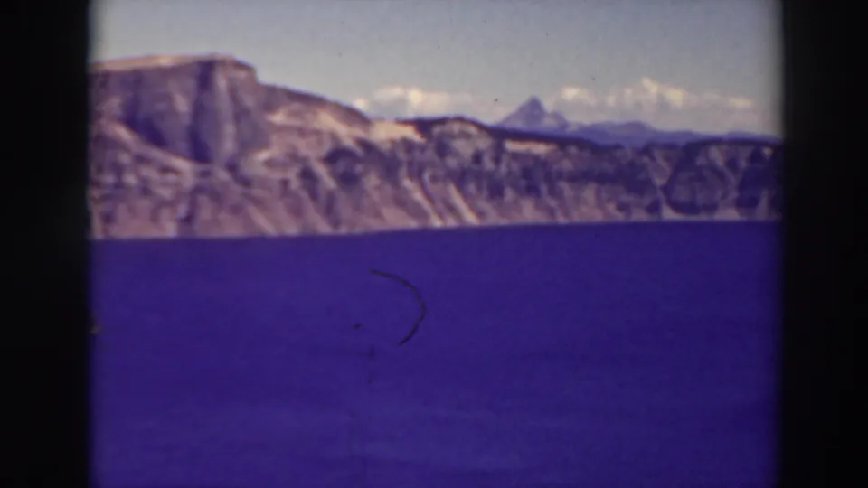 1937 8mm frame of Crater Lake's blue water and volcanic rim, with distant mountains and visible film wear.