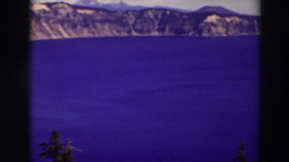 Crater Lake, Oregon, appears in a 1937 home-movie frame with blue water, distant rim cliffs, pale sky, and dark 8mm frame edges.