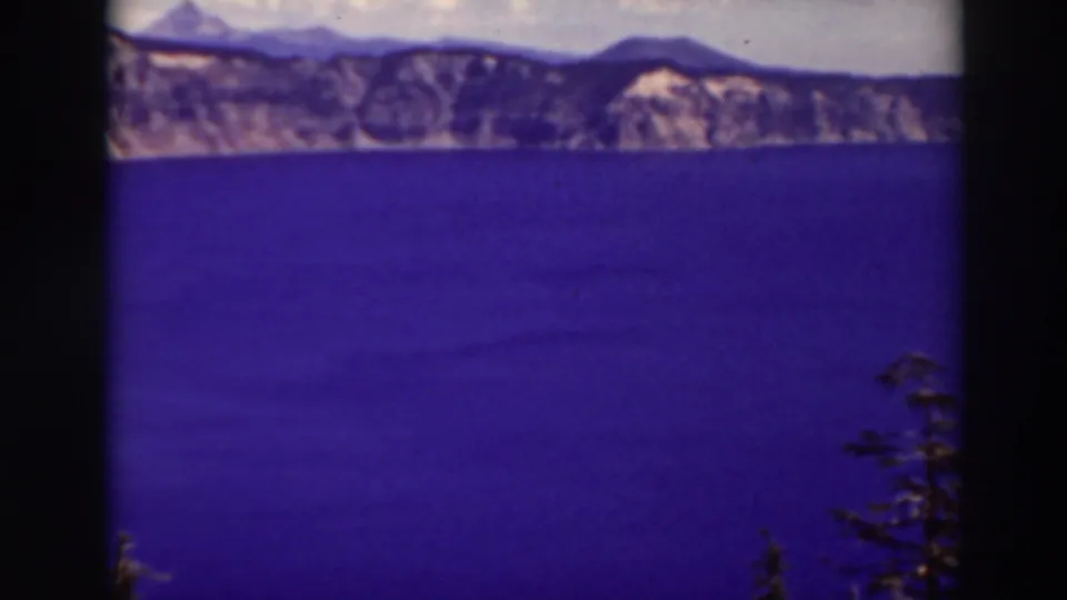 1937 Crater Lake footage shows deep blue water stretching toward rugged rim cliffs, with evergreen branches visible near the lower right edge.