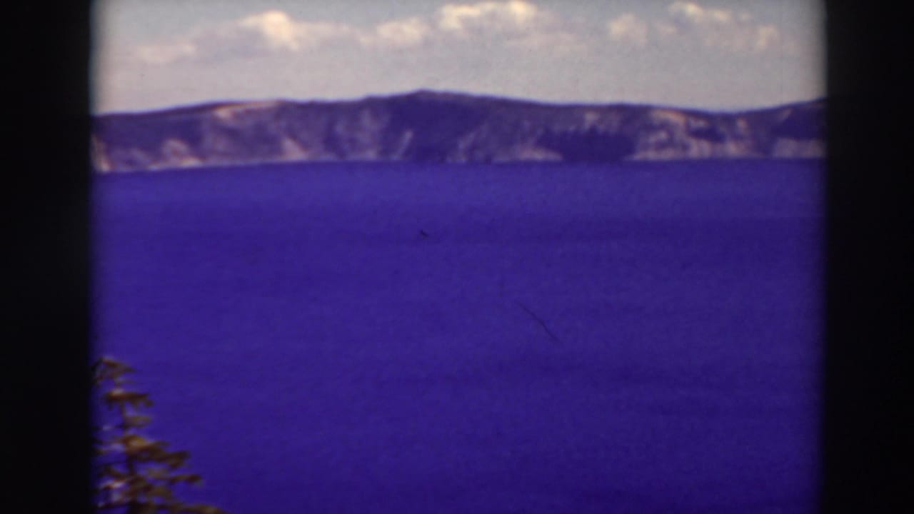 Wide blue lake, distant cliff rim, cloudy sky, and dark vertical film border down the center.