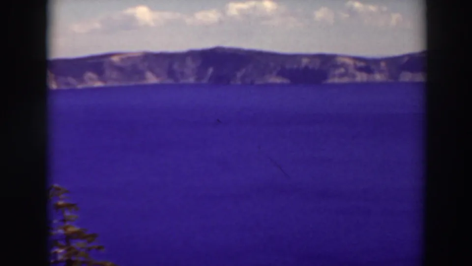 Crater Lake, Oregon appears in a 1937 home-movie frame with open blue water, far cliffs, sky, and visible 8mm frame borders.