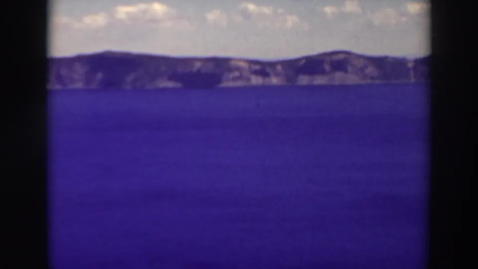 Crater Lake is seen across open blue water toward rugged rim cliffs in this 1937 8mm home-movie frame.