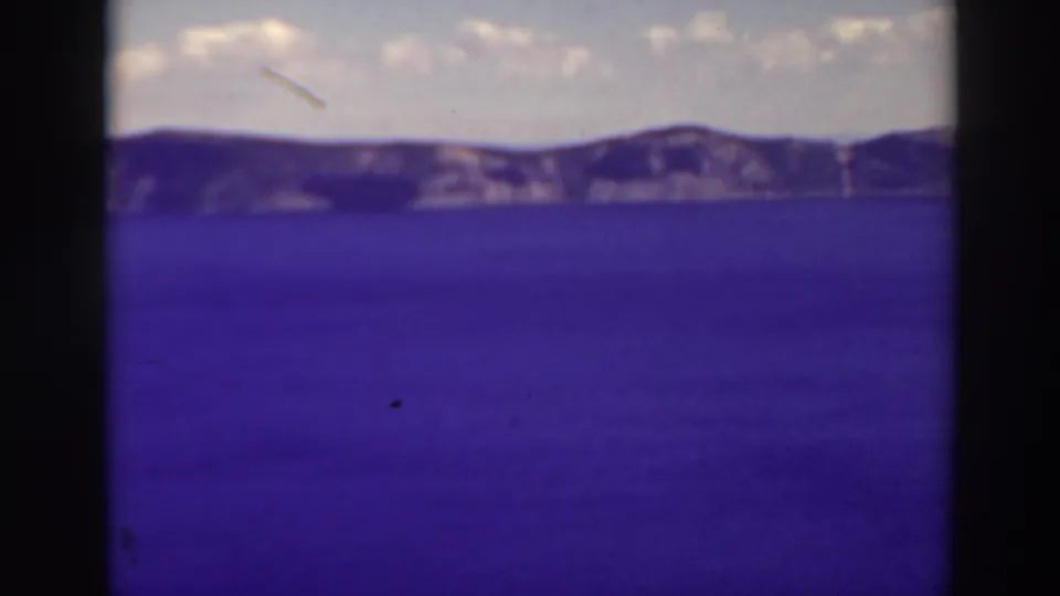 1937 8mm home-movie view of Crater Lake, Oregon, with blue water, distant rim slopes, pale clouds, and visible film gate edges.