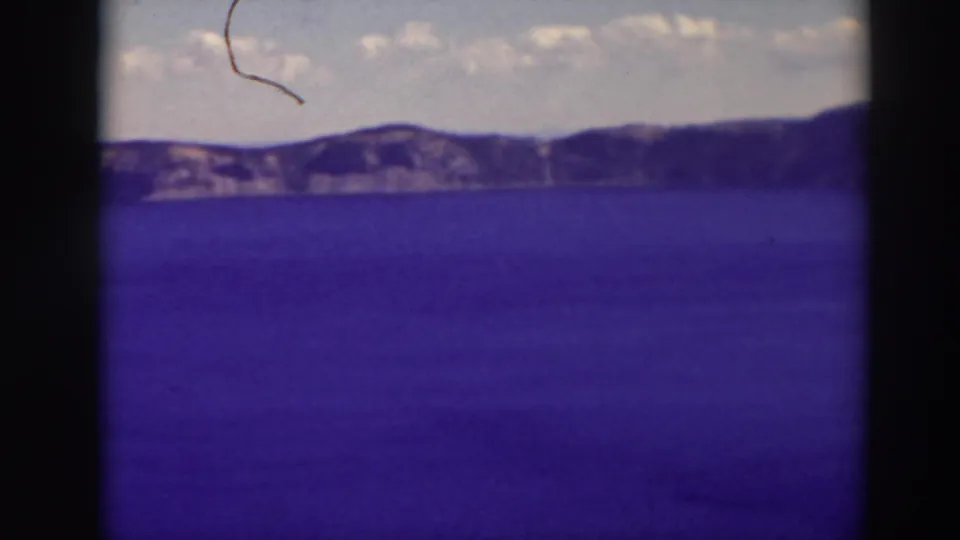 Visitor-shot 8mm view of Crater Lake in 1937, showing the lake surface, distant rim, pale cloud band, and a vertical film border.