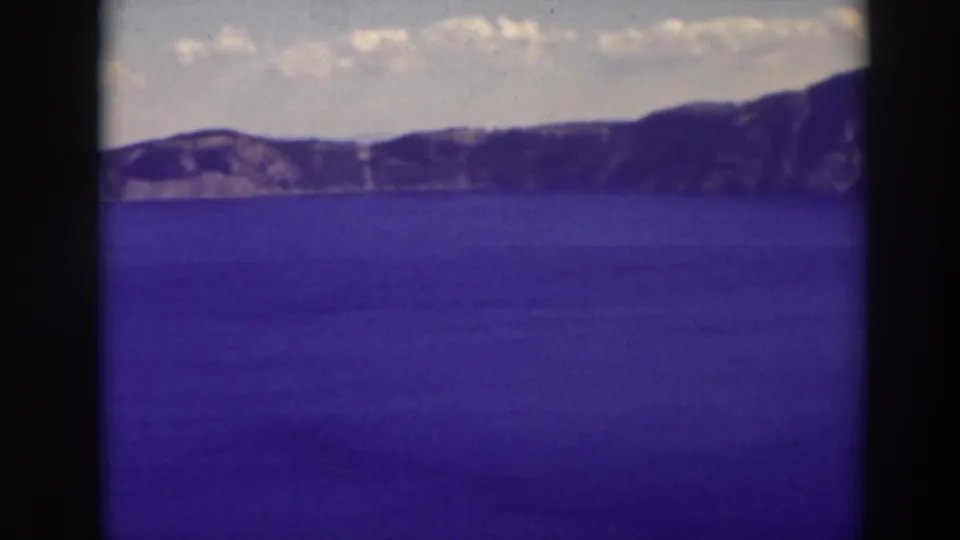 1937 8mm view of Crater Lake, Oregon, showing blue water and distant rim cliffs beneath scattered clouds.