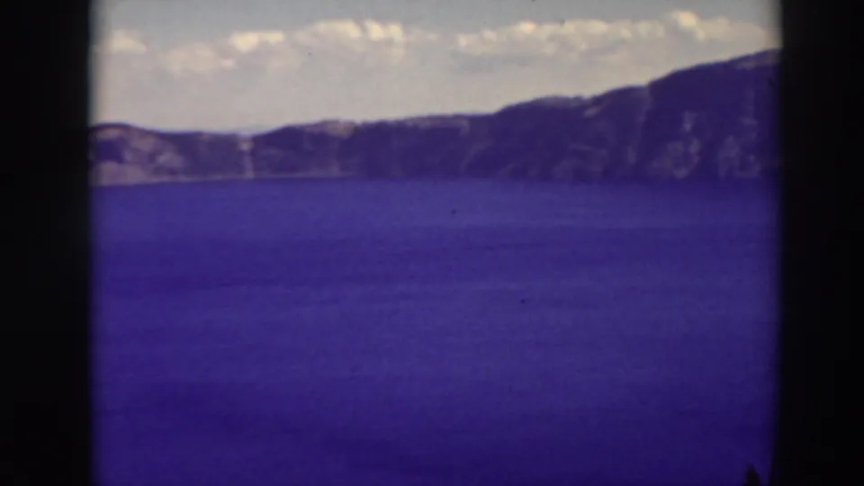 Crater Lake, Oregon, seen in a 1937 8mm frame with broad blue water, distant mountains, and visible film gate edges.