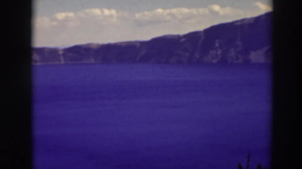 Wide 1937 home-movie view across Crater Lake toward rugged rim cliffs, with blue water filling most of the frame.