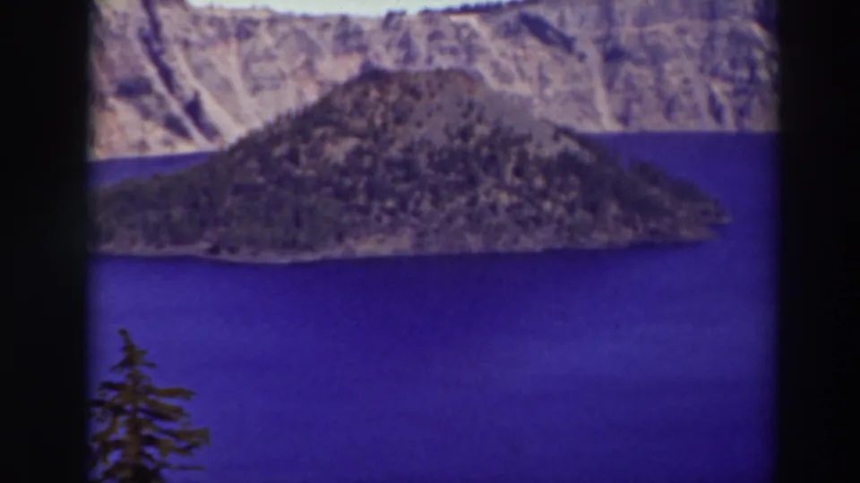 Archival 8mm frame from Crater Lake, Oregon, showing Wizard Island against blue water and rugged caldera walls.