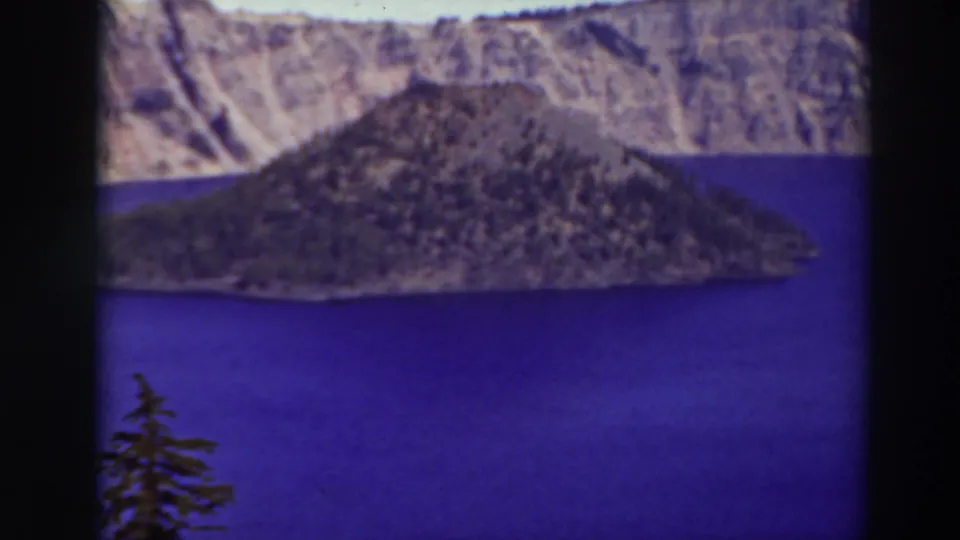 Late-1930s 8mm Crater Lake frame showing Wizard Island, saturated blue water, and distant caldera walls with film-edge shadows.