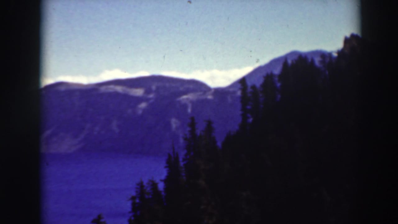 Blue lake and distant ridges framed by dark evergreen trees and film borders.