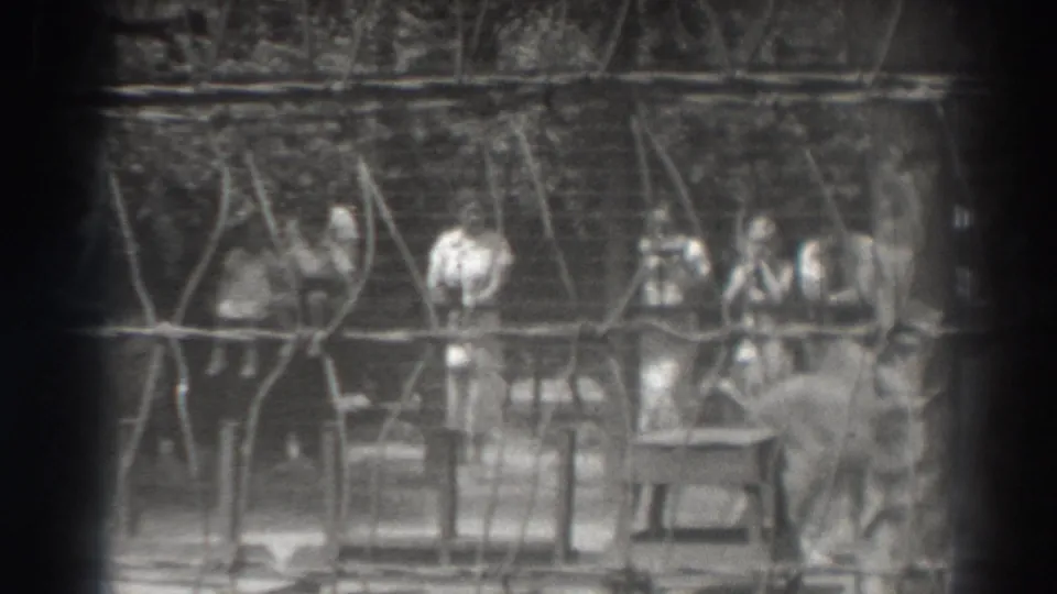 1937 El Monte home-movie frame showing visitors behind a wire barrier watching a lion inside a cage-like enclosure.
