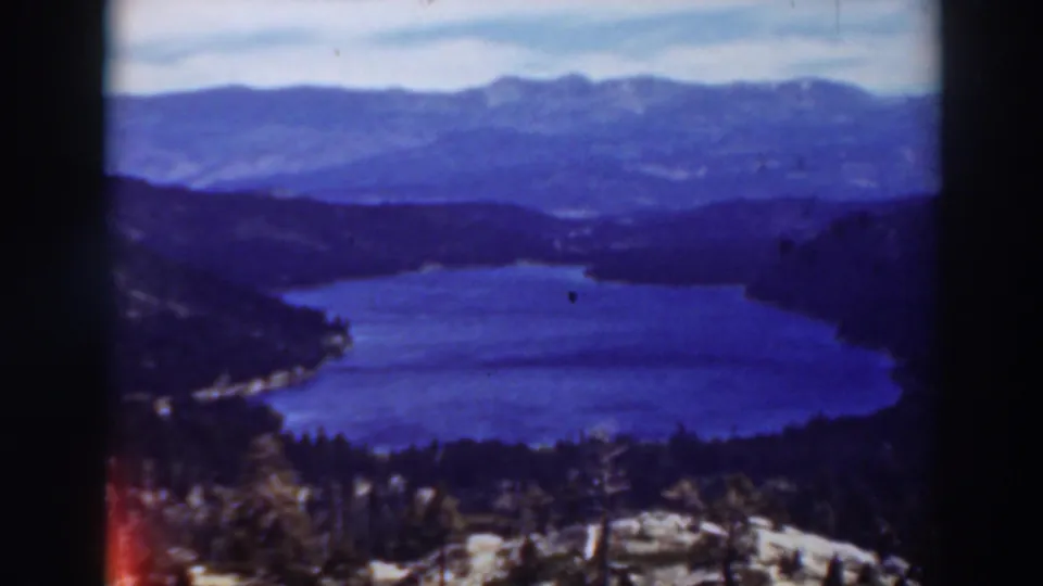 1937 Lake Tahoe home-movie frame showing blue water below dark wooded hills and distant mountain ranges under a pale sky.