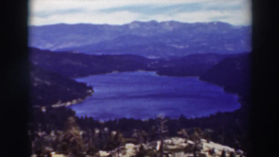 1937 Lake Tahoe frame with blue water, wooded slopes, distant ridgelines, and soft home-movie focus.