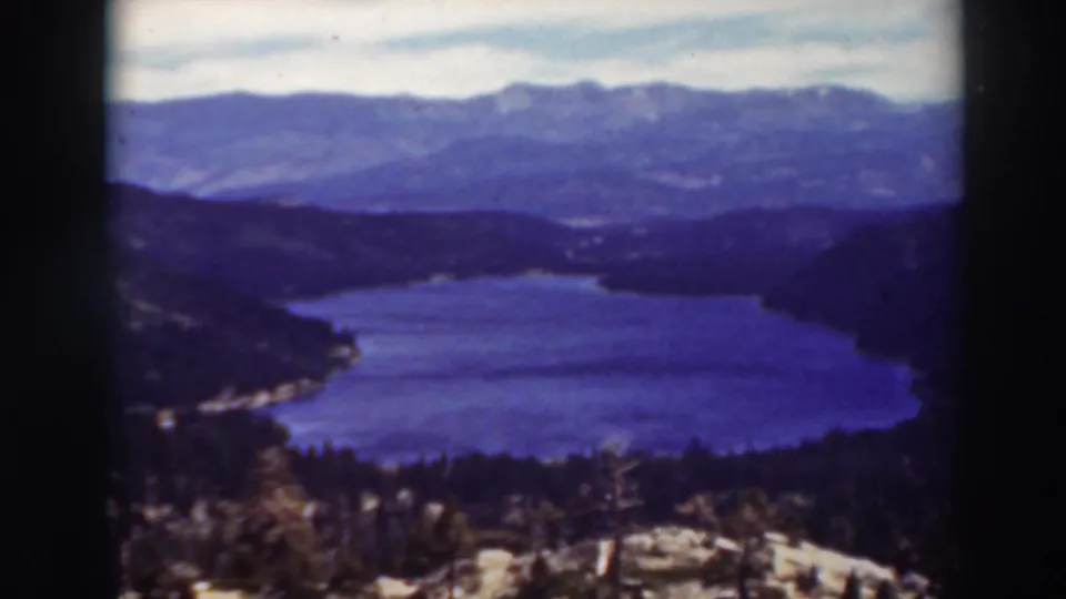 1937 Lake Tahoe home-movie frame showing the lake below a wooded overlook, with distant ridges softened by blue-purple film color.