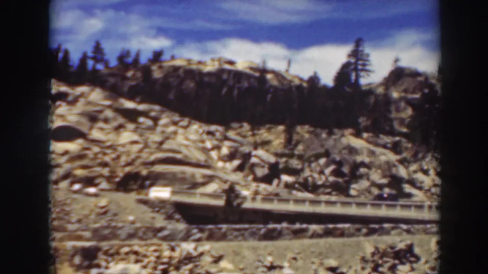 Lake Tahoe roadside terrain with exposed granite, scattered pines, and a small bridge or road cut through the slope.