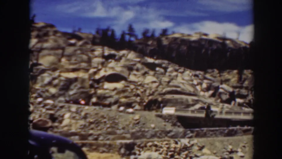 Lake Tahoe mountain road view with granite outcrops, pines, a small bridge, and soft 8mm frame edges.