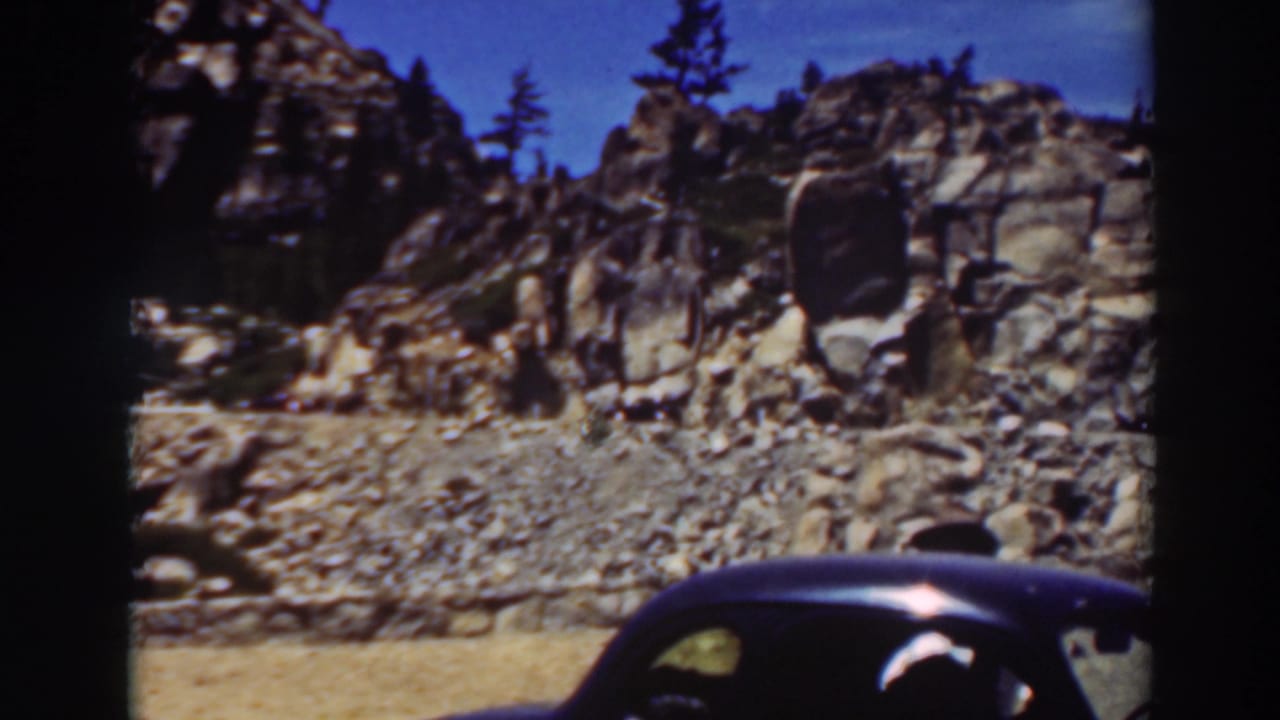 Rocky mountain roadside with the roof of a dark vintage car at the lower edge.