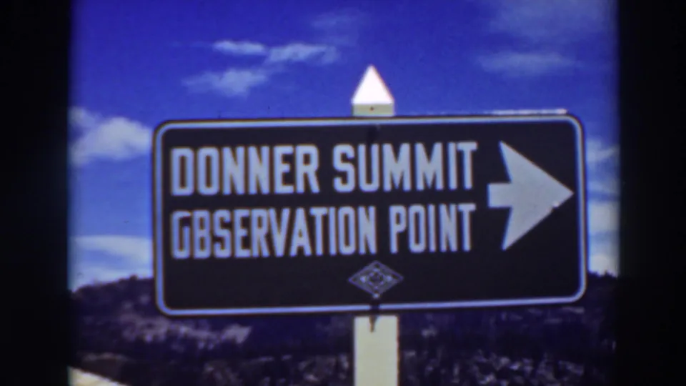 1937 Lake Tahoe-area 8mm frame of the Donner Summit Observation Point sign, with white lettering, right arrow, clouds, and hillside below.