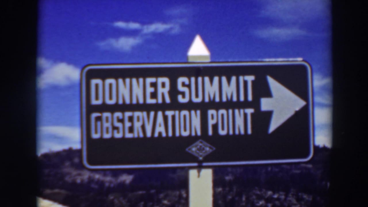 Black Donner Summit Observation Point sign with a right arrow against blue sky and hillside.