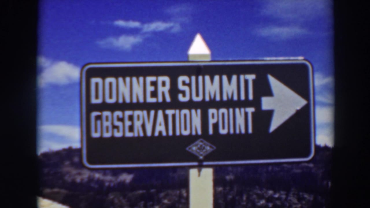 1937 8mm view of the Donner Summit Observation Point sign, with white lettering, a right arrow, and blue sky behind it.