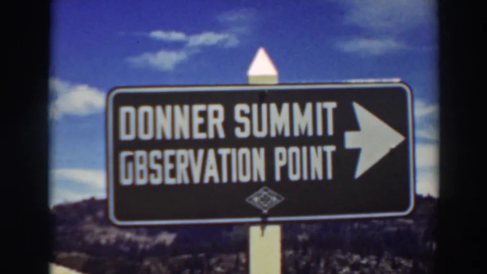 1937 color 8mm frame of a black Donner Summit Observation Point sign, white post, clouds, and dark mountain hillside.