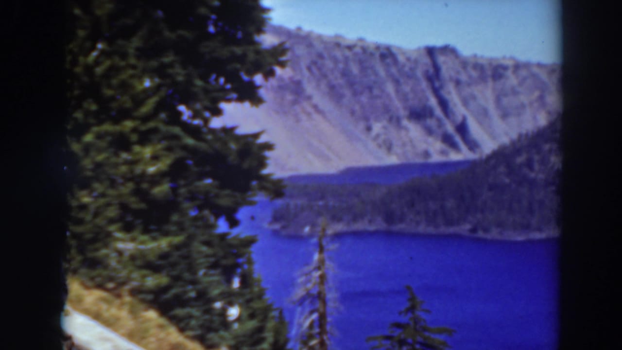 Lake and rocky mountains framed by evergreen trees and dark film edges.