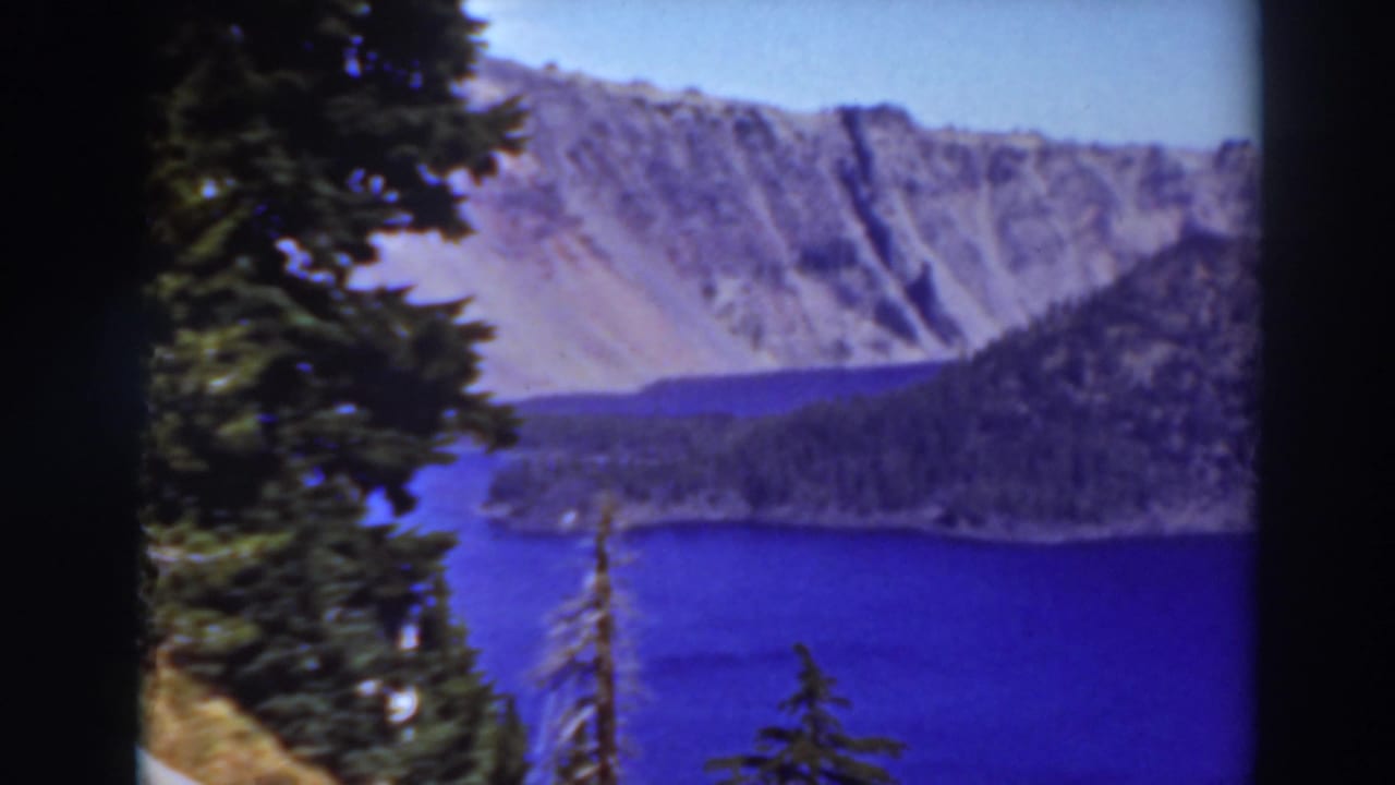 Lake Tahoe, California, seen through trees with deep blue water, a forested shore, and pale rocky mountain walls.