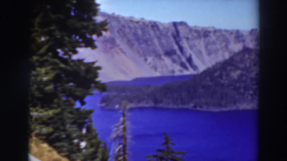 Lake Tahoe, California, seen through trees with deep blue water, a forested shore, and pale rocky mountain walls.