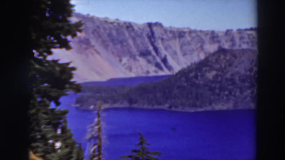 1937 8mm scenic frame of Lake Tahoe with foreground evergreens, blue water, wooded shoreline, and rugged mountain slopes.