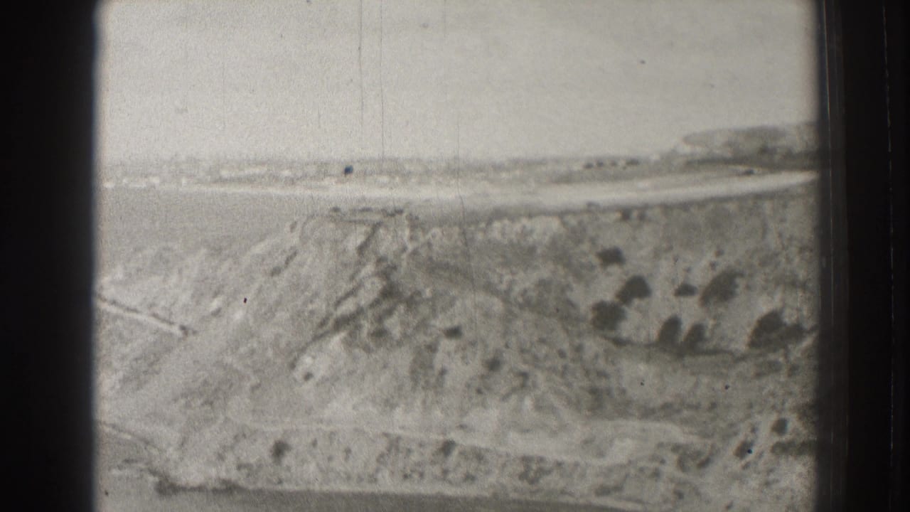 Black-and-white coastal bluff with ocean and distant shoreline beyond the frame edge.