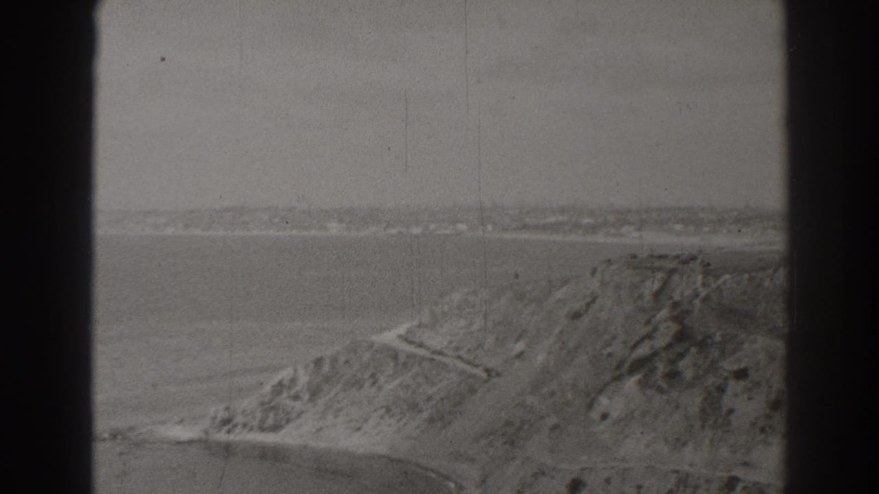 Coastal bluff above calm water with a winding path and distant shoreline.