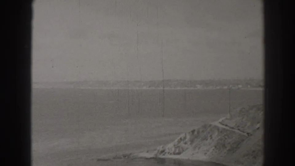 Soft 8mm frame from Long Beach showing open water, a partial coastal bluff, and a narrow path near the edge.