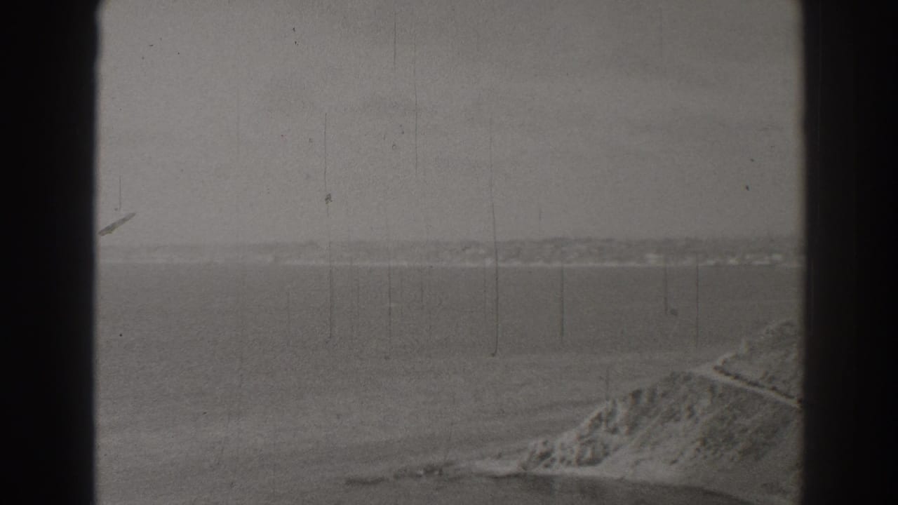 Hazy sea horizon with distant land and rocky shoreline framed by dark film borders.