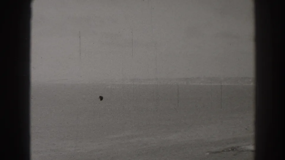 Archival Long Beach sea view with faint distant coastline, overcast sky, and visible 8mm film grain, scratches, and gate borders.
