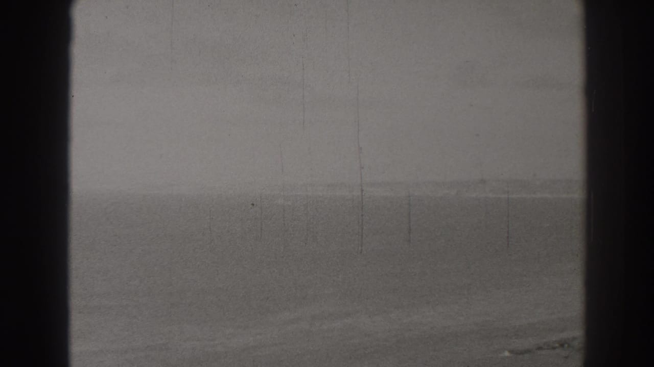 1937 8mm view over Long Beach, California, with ocean horizon, sandy foreground, and dark gate edges.