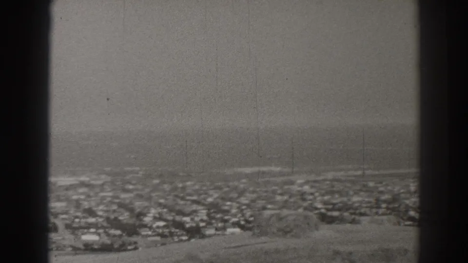 1937 Long Beach home-movie frame showing dense residential blocks below a hazy ocean horizon, bordered by dark film edges.