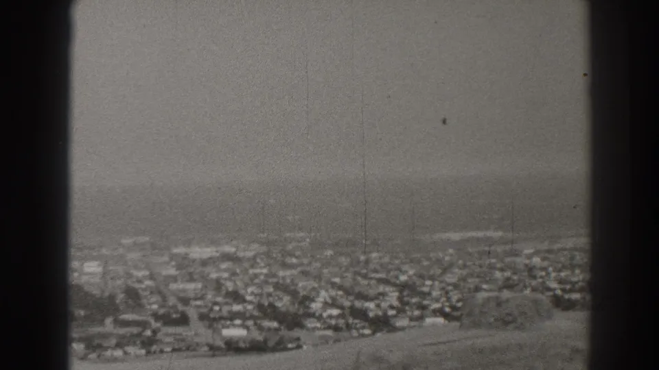 Black-and-white 8mm frame of Long Beach residential blocks extending toward the ocean, with soft focus and visible film wear.